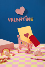 Front View Of The Words VALENTINE And Paper Hearts Pasted Onto A Blue Background. A Yellow Card Inside A Mini Cart, Surrounded By Sweets, Pens And Podiums,