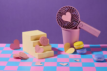 Cookies, Macarons And Paper Hearts Are Decorated On A Blue-pink Checkered Surface With A Platform, A Paper Cup And A Handheld Fan. Purple Background.