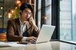 © Lumina Frame - Busy Asian young business man sales manager making phone call using laptop in office. Japanese businessman talking on cellphone working consulting client discussing online financial data,Generative AI