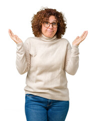 Canvas Print - Beautiful middle ager senior woman wearing turtleneck sweater and glasses over isolated background clueless and confused expression with arms and hands raised. Doubt concept.