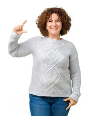 Wall Mural - Beautiful middle ager senior woman wearing winter sweater over isolated background smiling and confident gesturing with hand doing size sign with fingers while looking and the camera. Measure concept.