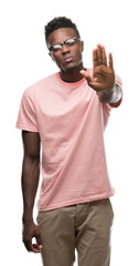 Sticker - Young african american man wearing pink t-shirt doing stop sing with palm of the hand. Warning expression with negative and serious gesture on the face.