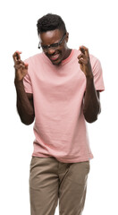 Wall Mural - Young african american man wearing pink t-shirt smiling crossing fingers with hope and eyes closed. Luck and superstitious concept.