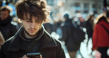 Young Man Standing Or Walking On A City Street, Looking At His Smartphone That He Is Holding In His Hands. Youthful Male Person Wearing A Black Coat, Teen Using Technology, Cellphone