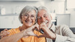 © Daniel - Close up portrait happy sincere middle aged elderly retired family couple making heart gesture with fingers, showing love or demonstrating sincere feelings together indoors, looking at camera..