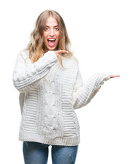 Poster - Beautiful young blonde woman wearing winter sweater over isolated background amazed and smiling to the camera while presenting with hand and pointing with finger.