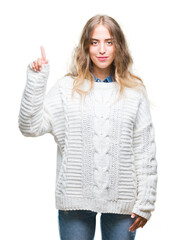 Poster - Beautiful young blonde woman wearing winter sweater over isolated background showing and pointing up with finger number one while smiling confident and happy.