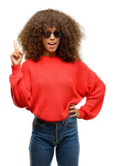 Wall Mural - African american woman wearing sunglasses happy and surprised cheering expressing wow gesture pointing up