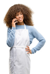 Sticker - African american shop owner woman wearing an apron happy talking using a smartphone mobile phone