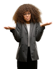 Canvas Print - African american business woman wearing glasses clueless and confused expression with arms and hands raised. Doubt concept.