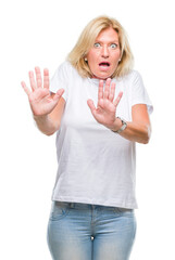 Canvas Print - Middle age blonde woman over isolated background afraid and terrified with fear expression stop gesture with hands, shouting in shock. Panic concept.