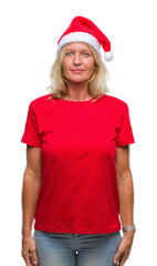 Canvas Print - Middle age blonde woman wearing christmas hat over isolated background with serious expression on face. Simple and natural looking at the camera.