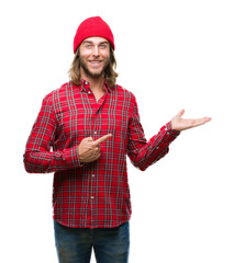 Sticker - Young handsome man with long hair wearing red cap over isolated background amazed and smiling to the camera while presenting with hand and pointing with finger.