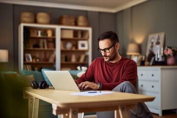 a young adult male freelance programmer deep in thought while typing on his laptop and working from 