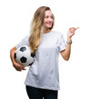 © Krakenimages.com - Young beautiful blonde woman holding soccer ball over isolated background very happy pointing with hand and finger to the side