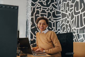 Wall Mural - Pretty female freelancer working on laptop while sitting on modern coworking background