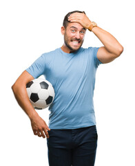 Poster - Young handsome man holding soccer football ball over isolated background stressed with hand on head, shocked with shame and surprise face, angry and frustrated. Fear and upset for mistake.