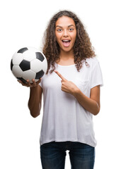 Canvas Print - Young hispanic woman holding soccer football ball very happy pointing with hand and finger