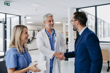 Pharmaceutical sales representative talking with doctors in medical building, shaking hands. Presenting new pharmaceutical product, drugs, medication.