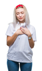 Wall Mural - Young blonde woman wearing headphones listening to music over isolated background smiling with hands on chest with closed eyes and grateful gesture on face. Health concept.