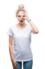 Sticker - Young beautiful blonde woman wearing white t-shirt over isolated background doing ok gesture shocked with surprised face, eye looking through fingers. Unbelieving expression.