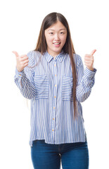 Sticker - Young Chinese woman over isolated background success sign doing positive gesture with hand, thumbs up smiling and happy. Looking at the camera with cheerful expression, winner gesture.