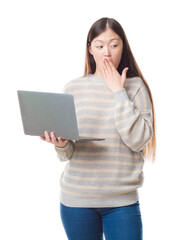 Wall Mural - Young Chinese woman over isolated background using computer laptop cover mouth with hand shocked with shame for mistake, expression of fear, scared in silence, secret concept