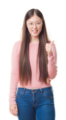 Sticker - Young Chinese woman over isolated background wearing glasses doing happy thumbs up gesture with hand. Approving expression looking at the camera with showing success.