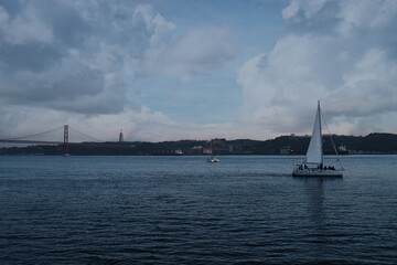 Wall Mural - Beautiful landscape with a yacht sailing the Tejo River with the Bridge Ponte 25 de Abril view in Lisbon, Portugal