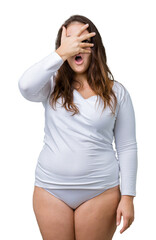 Beautiful plus size young overwight woman wearing white underwear over isolated background peeking in shock covering face and eyes with hand, looking through fingers with embarrassed expression.