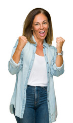 Canvas Print - Middle age adult woman wearing casual denim shirt over isolated background very happy and excited doing winner gesture with arms raised, smiling and screaming for success. Celebration concept.