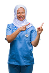 Sticker - Middle age senior arab nurse woman wearing hijab over isolated background smiling and looking at the camera pointing with two hands and fingers to the side.