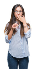 Wall Mural - Young asian woman drinking a glass of water over isolated background cover mouth with hand shocked with shame for mistake, expression of fear, scared in silence, secret concept