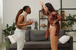 © pressmaster - Side view of two young angry girlfriends shouting at one another and gesturing by hands while standing by couch during argument