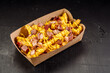 Delicious fast food French fries with bacon and cheese sauce in a take-out cardboard box