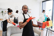© sofiko14 - Portrait of young African American man professional cleaning worker pointing on bucket for washing with detergents on bright kitchen studio background, copy space.