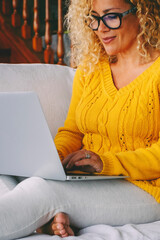 Wall Mural - Pretty middle age woman writing on laptop and smiling. Single lady using computer alone at home. Blonde female adult enjoy leisure time with wireless notebook connection sitting and relaxing