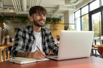 Young man in plaid shirt sitting at laptop and having a video call