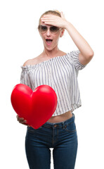 Canvas Print - Blonde teenager woman holding red heart stressed with hand on head, shocked with shame and surprise face, angry and frustrated. Fear and upset for mistake.