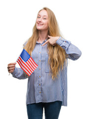 Sticker - Blonde teenager woman holding flag of United States of America with surprise face pointing finger to himself