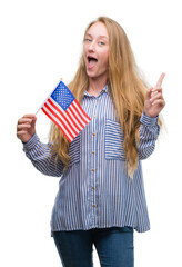 Sticker - Blonde teenager woman holding flag of United States of America surprised with an idea or question pointing finger with happy face, number one