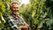 Standing amidst luscious grapevines in his vineyard is an elderly man wearing a lovely grin.
