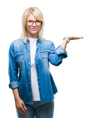 Poster - Young beautiful blonde woman wearing glasses over isolated background smiling cheerful presenting and pointing with palm of hand looking at the camera.