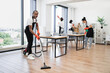 © sofiko14 - Professional service team of cleaning company. Young adult African American man wearing black apron and red rubber gloves vacuuming floor of modern light office.