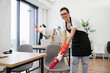 © sofiko14 - Happy smiling multicultural employees of company cleaning in bright, spacious modern office. Multiethnic young female cleaner vacuuming chair with portable cordless vacuum cleaner, looking at camera.