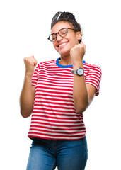 Sticker - Young braided hair african american girl wearing glasses over isolated background very happy and excited doing winner gesture with arms raised, smiling and screaming for success. Celebration concept.