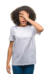 Canvas Print - Young afro american woman over isolated background peeking in shock covering face and eyes with hand, looking through fingers with embarrassed expression.