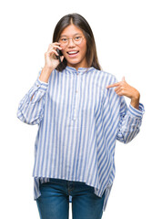 Poster - Young asian woman speaking on the phone over isolated background with surprise face pointing finger to himself