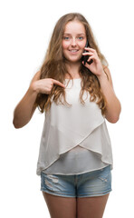 Wall Mural - Young blonde woman using smartphone with surprise face pointing finger to himself