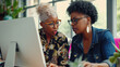 © Oulaphone - Startup mature black business woman sharing her expertise with her colleague as they collaborate on a project using a computer.